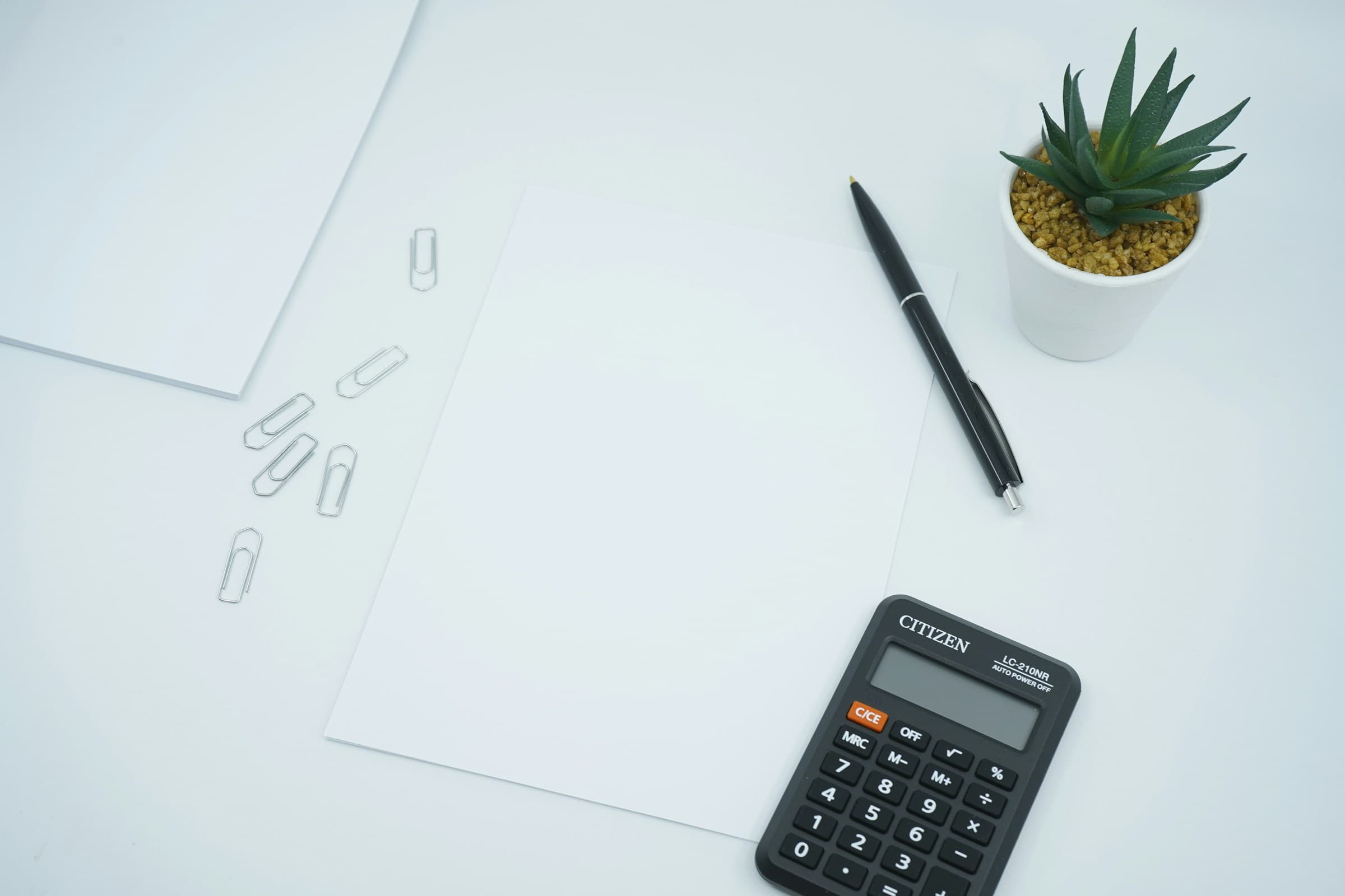 Calculadora, pluma y hojas en blanco sobre un escritorio