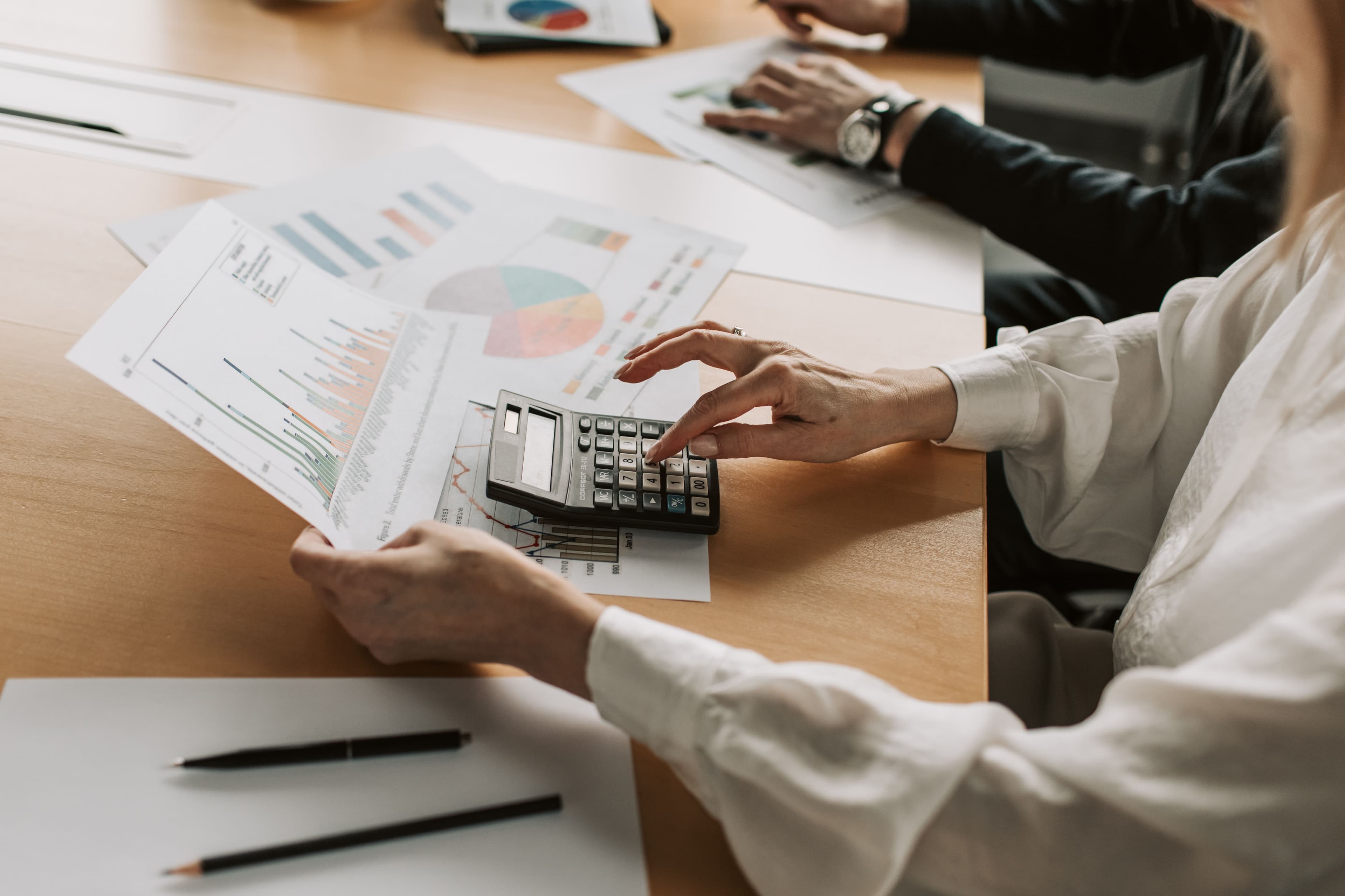 Manos revisando gráficas financieras con una calculadora sobre el escritorio